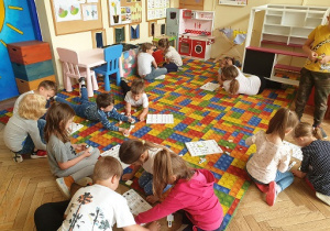Zdjęcie przedstawia grupę dzieci siedzących w małych grupach wykonujących zadanie